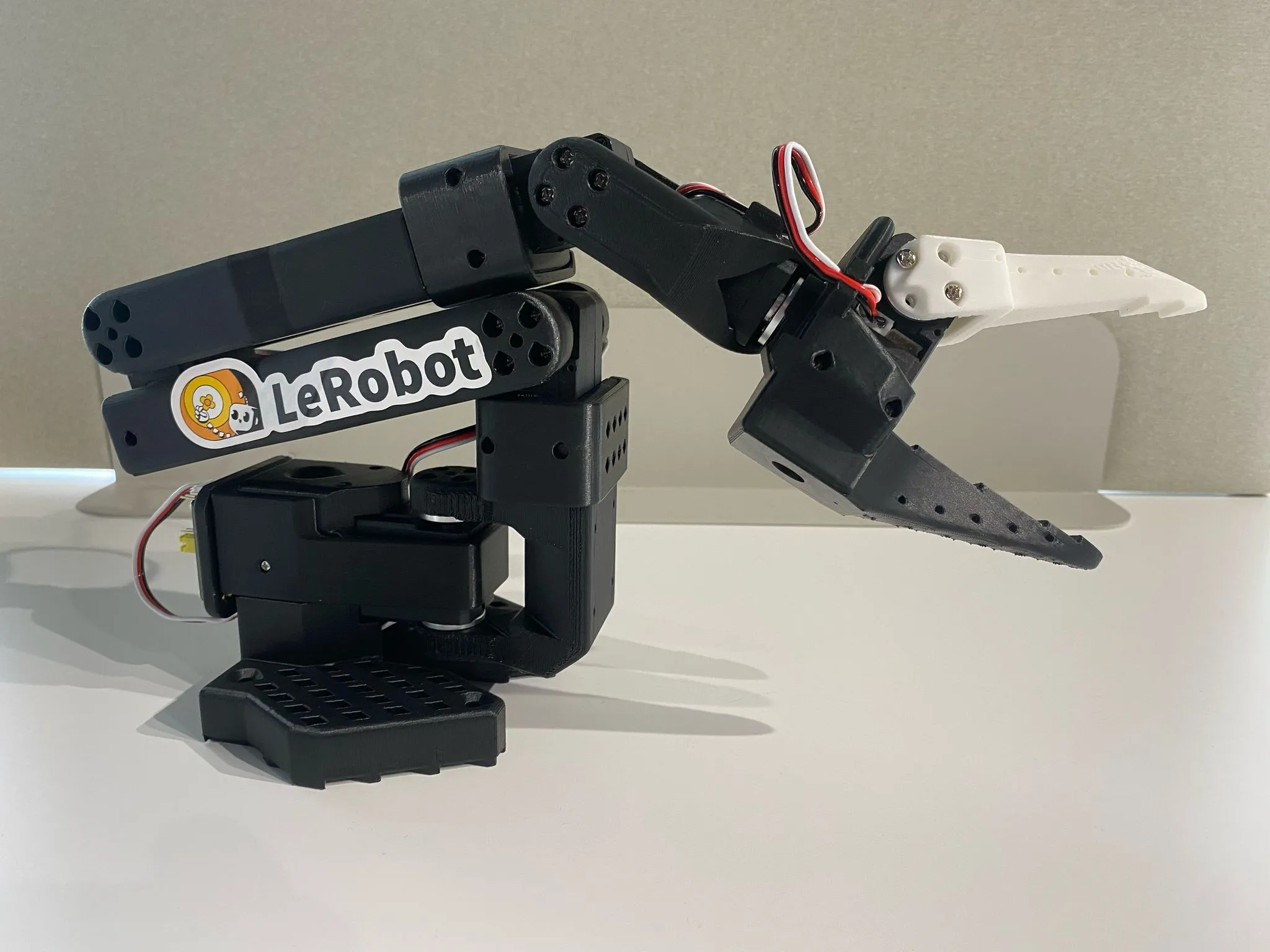 Black SO-101 follower arm with a parallel gripper, on a white table
